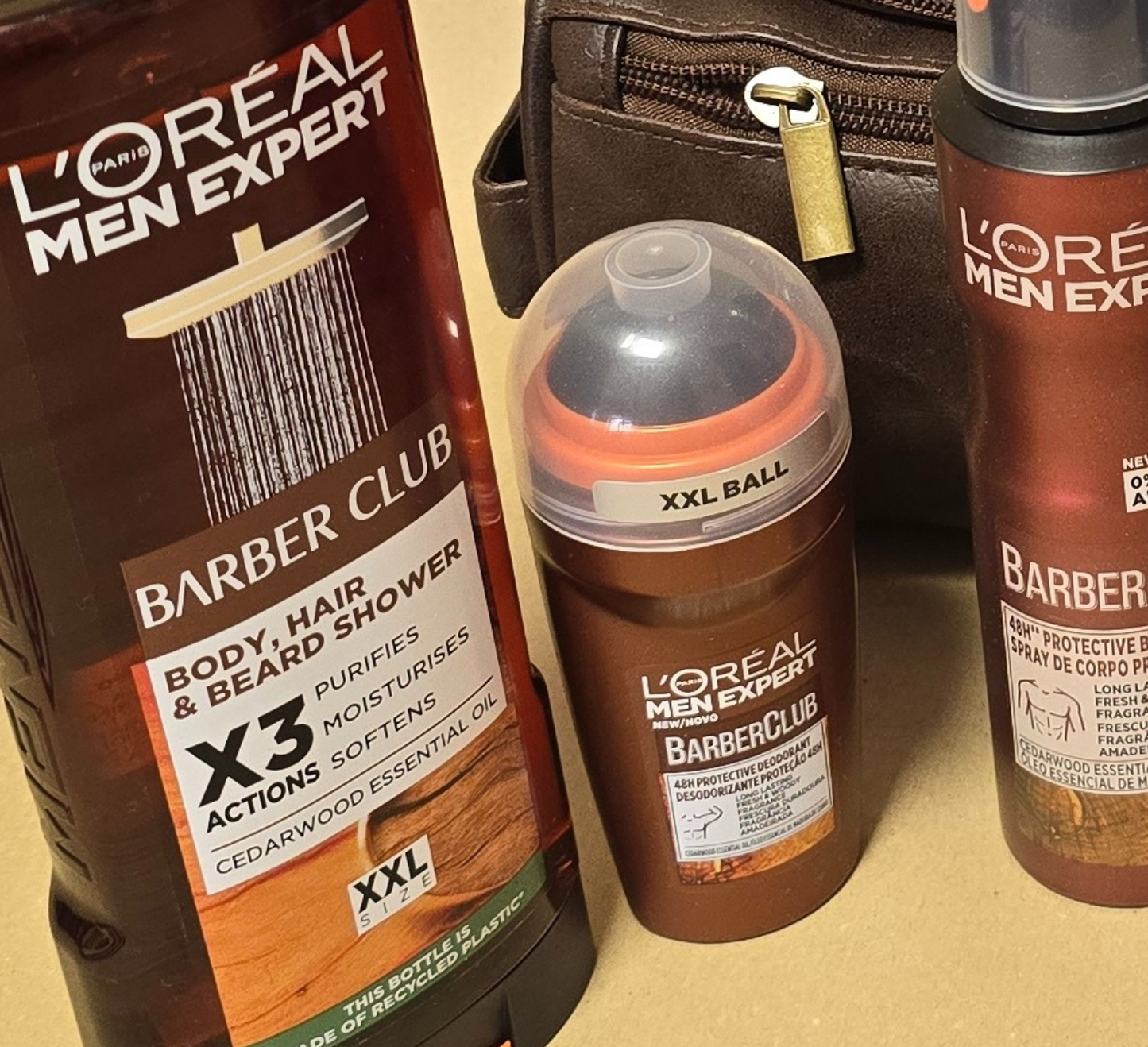 Men’s grooming and travel gift set in a brown leather Legacy toiletry bag filled with premium grooming essentials including deodorant, shower gel, shampoo, razors, and a rolled towel, styled on a wooden background with warm lighting.