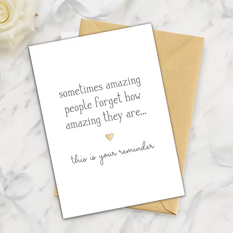 Minimalist inspirational greeting card with the quote “sometimes amazing people forget how amazing they are… this is your reminder” displayed beside a kraft envelope on a marble background.