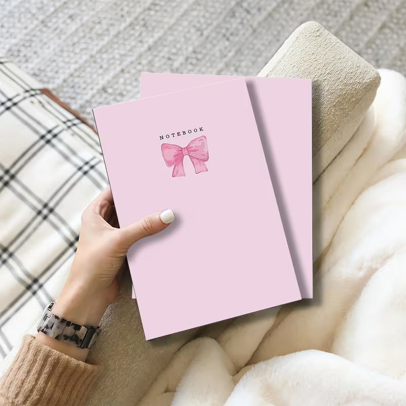 Cute pink notebook with elegant bow design and feminine aesthetic displayed on a neutral background.