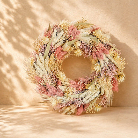 Luxury gift basket featuring a dried floral wreath, pink ceramic mug, wooden house keepsake, marshmallow gift box, and decorative home plaque arranged in a woven basket with a pink ribbon.