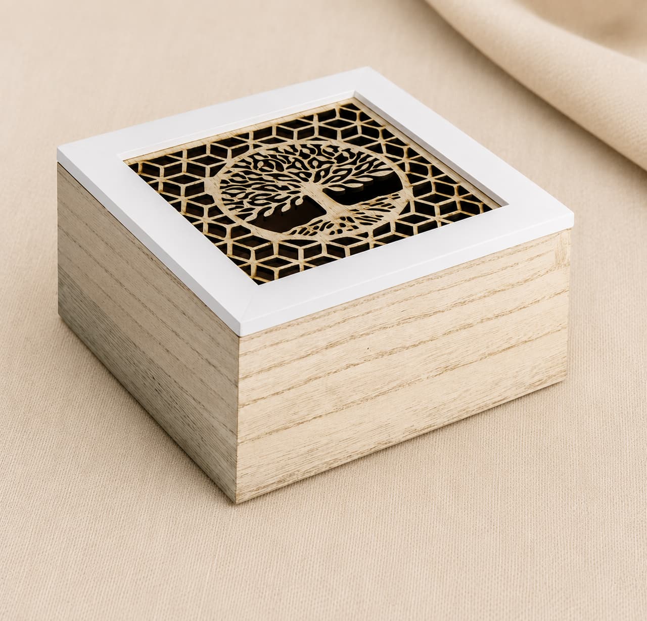 A square wooden babies keepsake box with a light natural wood grain body and a white-trimmed lid featuring a laser-cut gold tree of life design over a black geometric background, set on a beige fabric surface.