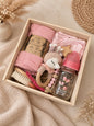 Pink newborn baby gift box in wooden keepsake box with muslin blanket, cotton onesie, brush, rattle and glass bottle.