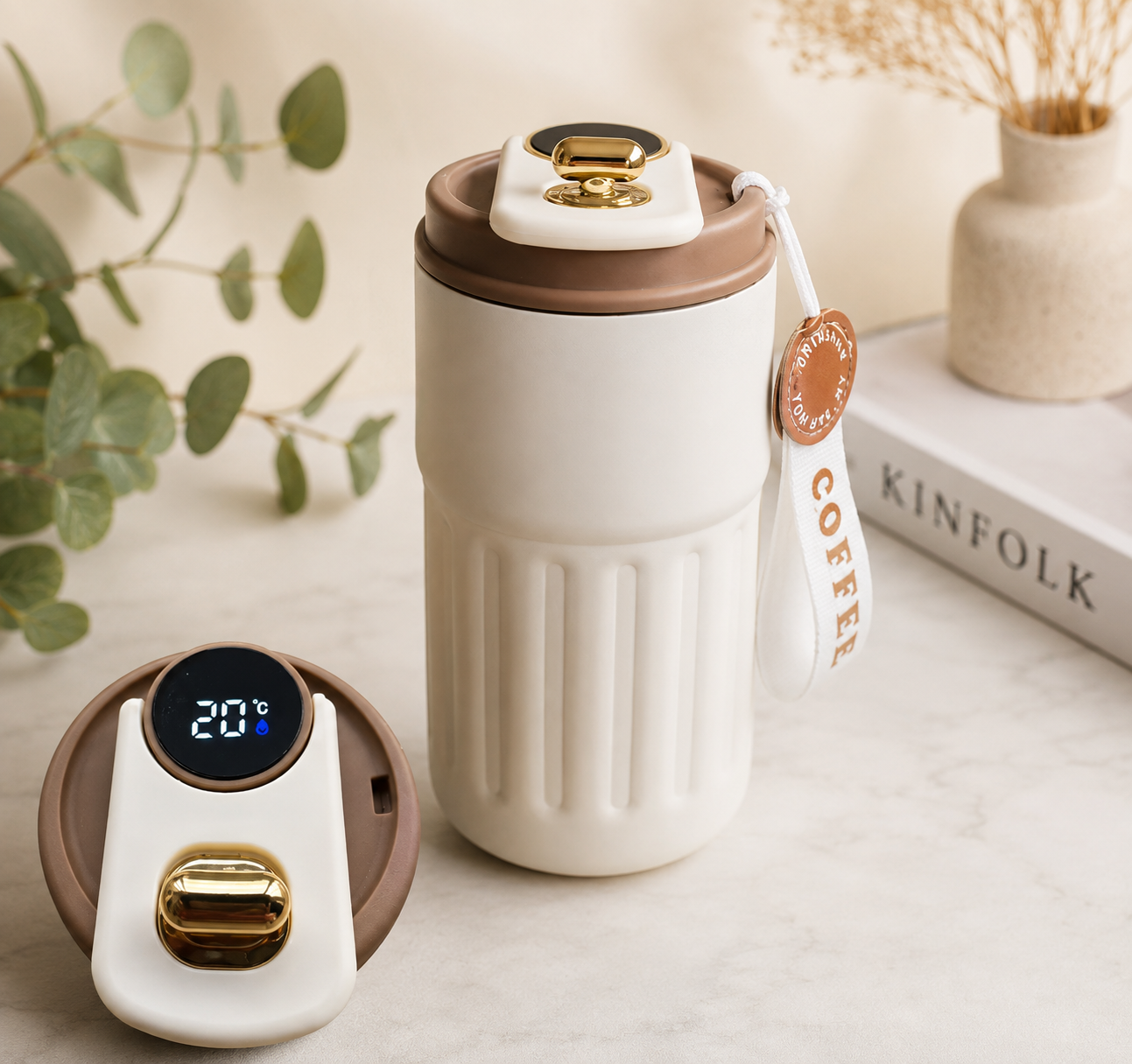 Cream and brown travel coffee tumbler with digital temperature display lid, gold accents, and white carrying strap on a neutral background.