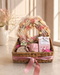 Luxury gift basket featuring a dried floral wreath, pink ceramic mug, wooden house keepsake, marshmallow gift box, and decorative home plaque arranged in a woven basket with a pink ribbon.