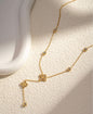 Gold necklace with clover-shaped pendant and crystal accents, featuring a delicate chain and drop detail on a neutral background.