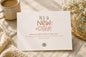 Card with 'It's a New Day!' message on a table with a cup of coffee and flowers.