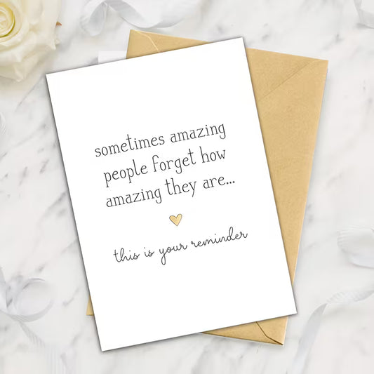Minimalist inspirational greeting card with the quote “sometimes amazing people forget how amazing they are… this is your reminder” displayed beside a kraft envelope on a marble background.