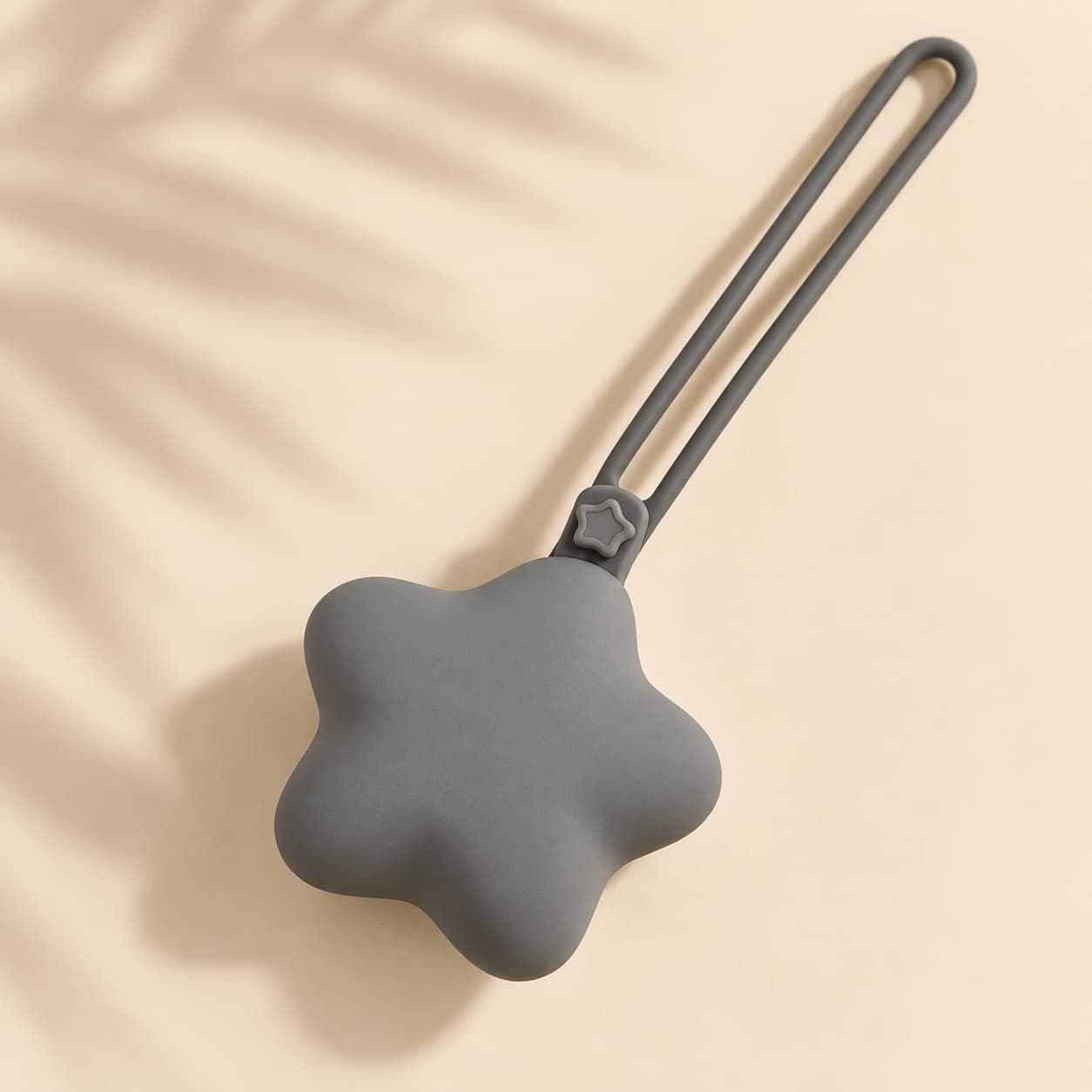 Grey star-shaped silicone case with long loop strap on a warm beige boho-minimal background.