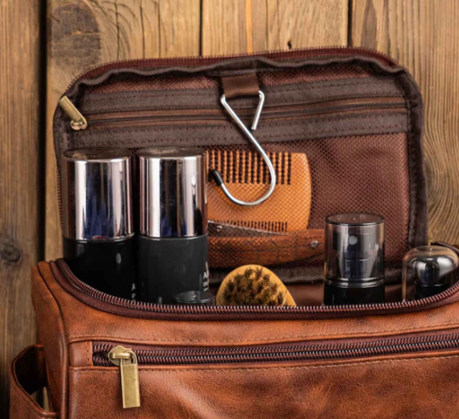 Men’s grooming and travel gift set in a brown leather Legacy toiletry bag filled with premium grooming essentials including deodorant, shower gel, shampoo, razors, and a rolled towel, styled on a wooden background with warm lighting.