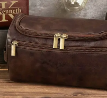 Men’s grooming and travel gift set in a brown leather Legacy toiletry bag filled with premium grooming essentials including deodorant, shower gel, shampoo, razors, and a rolled towel, styled on a wooden background with warm lighting. Gifting CY gift online shop cyprus and europe