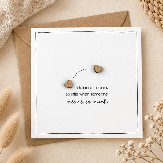 Minimal white greeting card with wooden hearts and the message “distance means so little when someone means so much” on a neutral boho background.