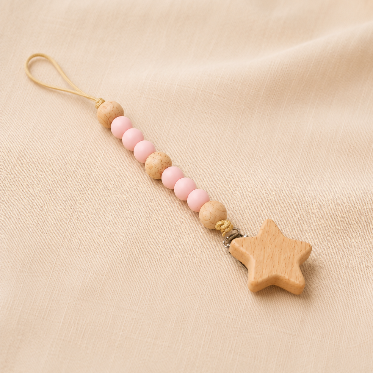 Pink and natural wooden bead pacifier clip with wooden star charm on cream fabric.
