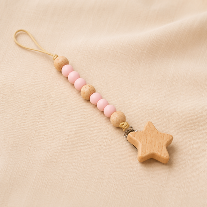 Pink and natural wooden bead pacifier clip with wooden star charm on cream fabric.
