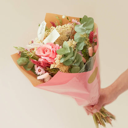 Bouquet of flowers wrapped in pink paper held by a person on a light background