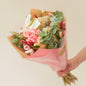 Bouquet of flowers wrapped in pink paper held by a person on a light background