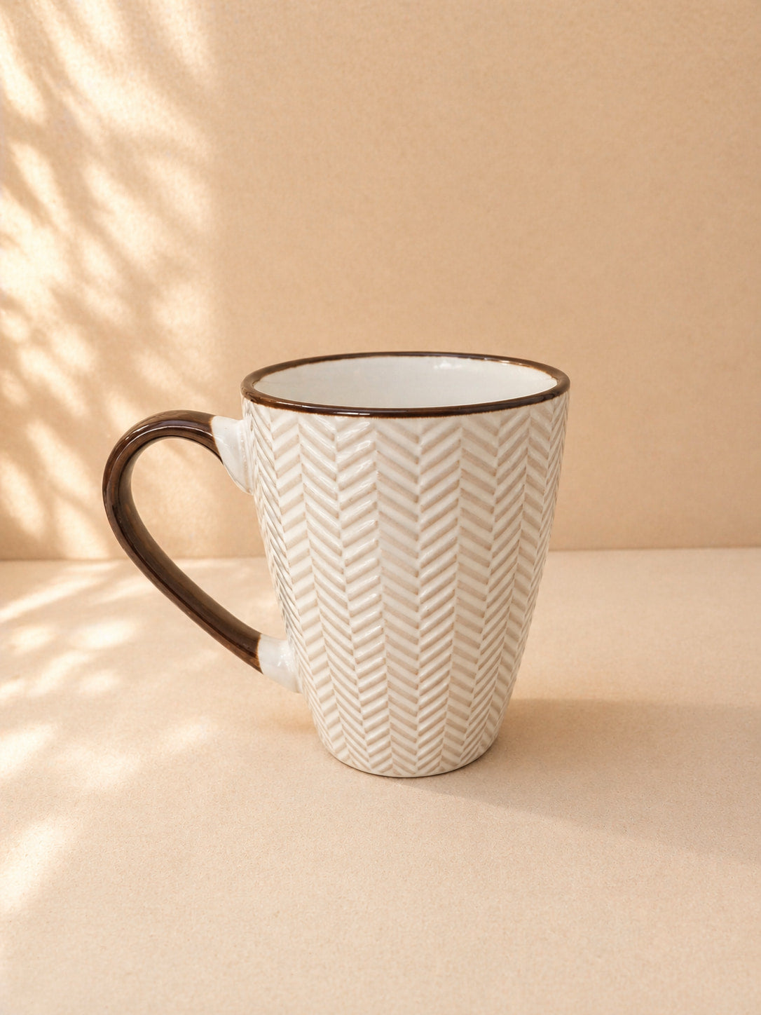 Ceramic mug with brown handle and chevron pattern on a beige background