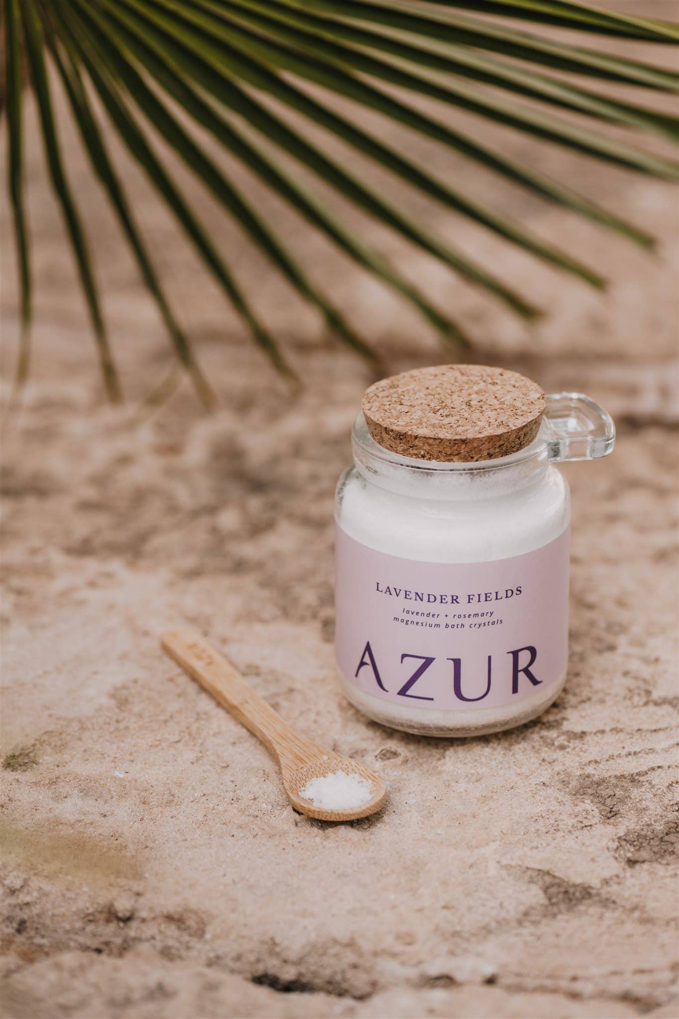 Jar of 'Azur' salt with a wooden spoon on a textured surface with palm leaves in the background