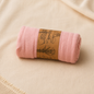 Rolled soft pink muslin baby blanket with kraft paper packaging on neutral beige fabric.
