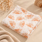 Soft white muslin baby swaddle blanket with warm orange sun print styled on a neutral boho-minimal background.