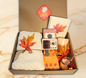 Amber Serenity Collection autumn gift box featuring a knitted blanket, M&S Rooibos tea, retro speaker, leaf notebook, and amber jar candle.