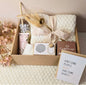 “A beautifully arranged ‘Best Mom Ever’ gift box containing a cozy cream blanket tied with a ribbon, floral hand cream, reusable tumbler, gold coffee spoon, mini speaker, Coffeeway coffee box, and a greeting card that says ‘Awesome people make awesome babies,’ surrounded by soft pink flowers