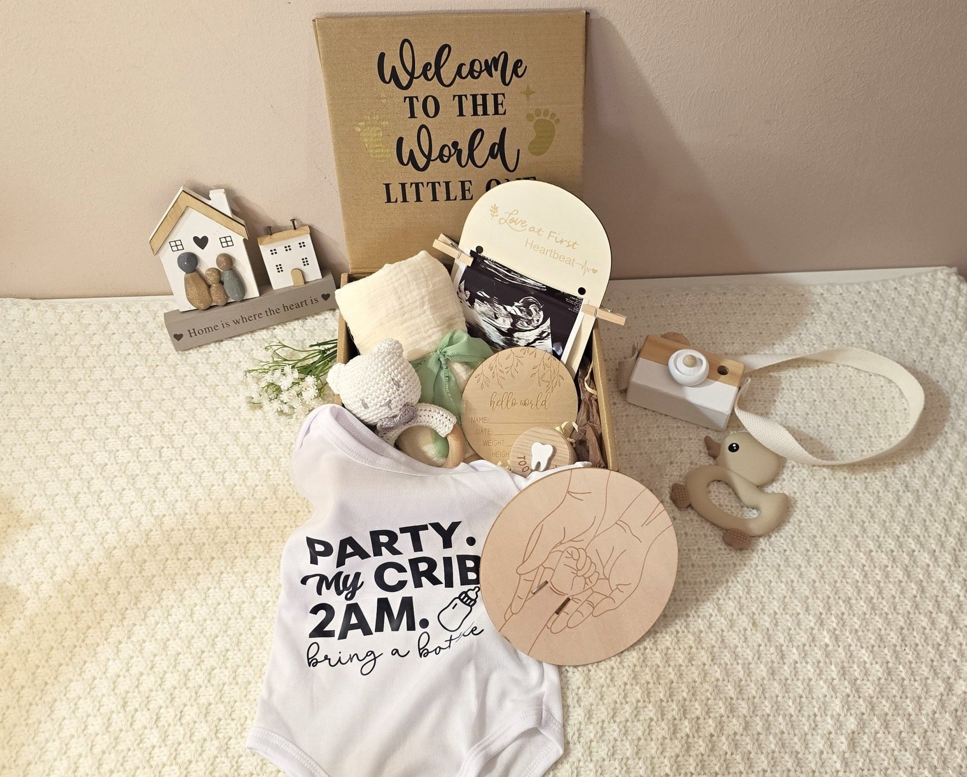 Welcome Little One newborn keepsake gift box with a funny onesie, crocheted bear, swaddle, 'Hello World' milestone disc, and 'First Tooth' box.