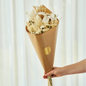 Bouquet of dried flowers wrapped in brown paper with a gold circle, held against a white curtain background.