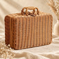 Woven wicker suitcase with twin handles, brown top strap and metal-tone details on a neutral boho background