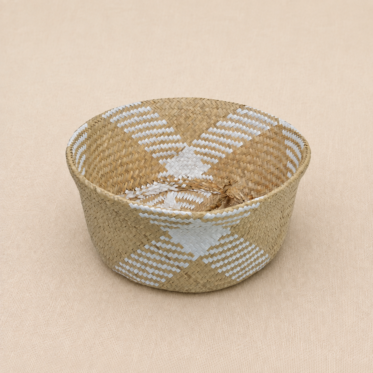 Handwoven natural seagrass baby basket with white geometric detailing on a soft ivory linen background.