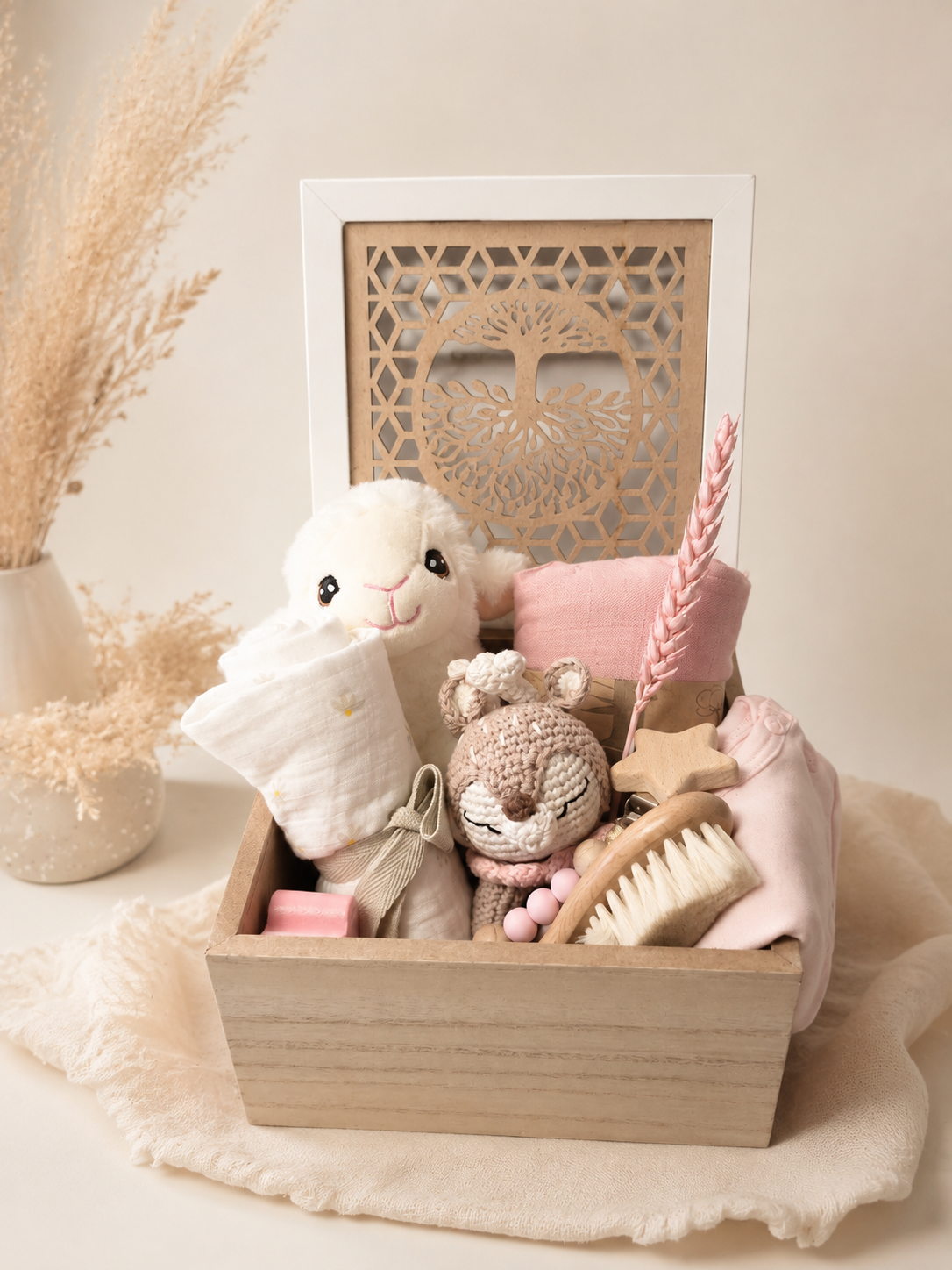 Neutral baby gift box with plush toy, wooden reindeer teether, baby hair brush, onesie, muslin blankets, pacifier clip, and Tree of Life wooden box.