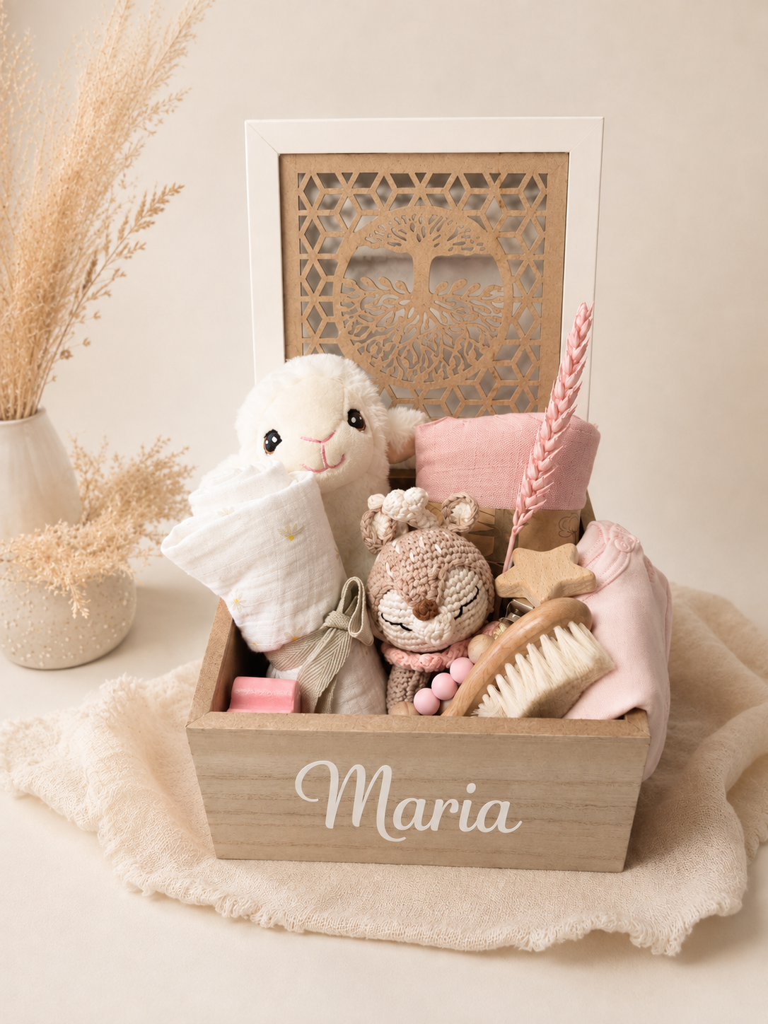 Neutral baby gift box with plush toy, wooden reindeer teether, baby hair brush, onesie, muslin blankets, pacifier clip, and Tree of Life wooden box.