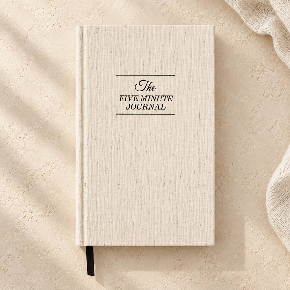 Beige textured hardcover Five Minute Journal with black cover lettering and a black ribbon bookmark.