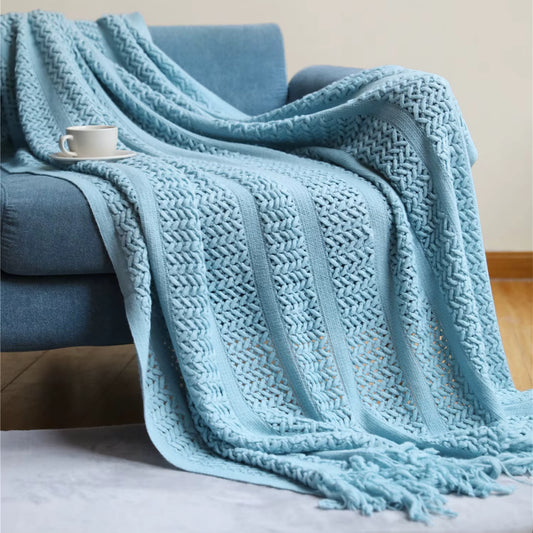 blue  knitted throw blanket with decorative fringe draped over a blue armchair, creating a cosy and elegant home setting.