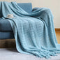 blue  knitted throw blanket with decorative fringe draped over a blue armchair, creating a cosy and elegant home setting.