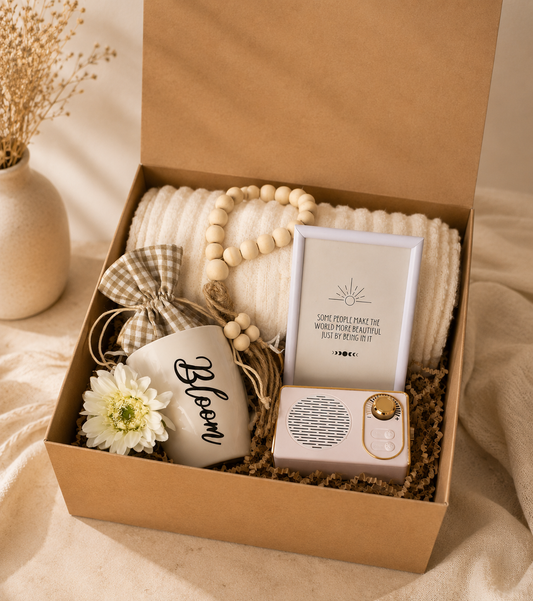 Boho self-care gift box featuring a cream blanket, Bloom mug, retro Bluetooth speaker, inspirational quote frame, and decorative accessories arranged in a luxury kraft gift box.