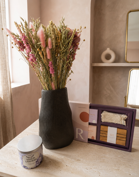 Luxury gift collection featuring a dried flower arrangement, decorative vase, scented candle, and self-care gift set styled in a warm and elegant interior setting.