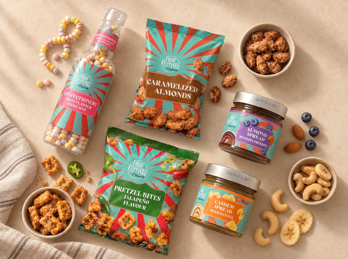 A styled flat-lay of Fresh Festival snack products on a beige surface, including a candy bottle, caramelized almonds bag, pretzel bites bag, lemonade spread jar, cashew spread jar, and nuts in bowls.