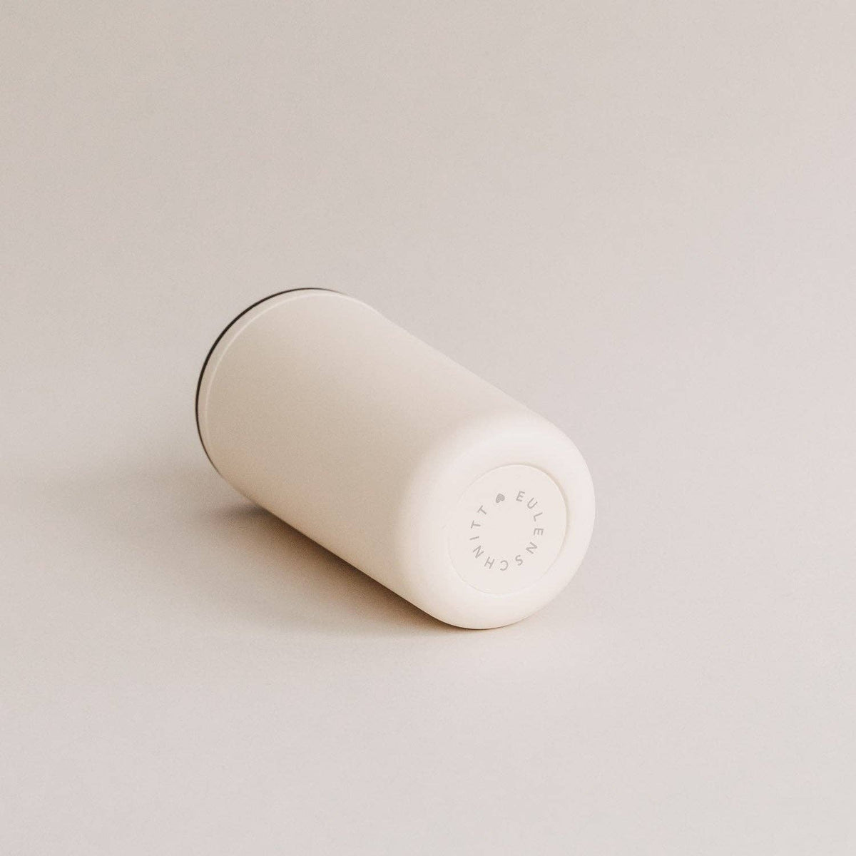 Cream travel cup lying on its side, showing its circular base.