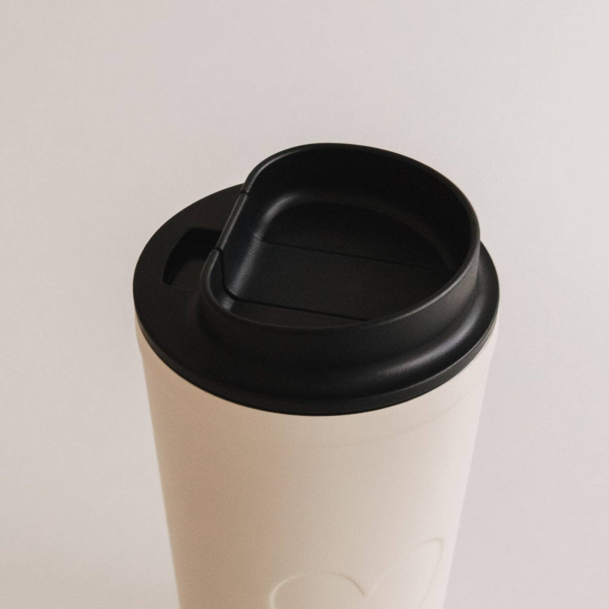 Close-up of the black drinking lid on the cream heart travel cup.