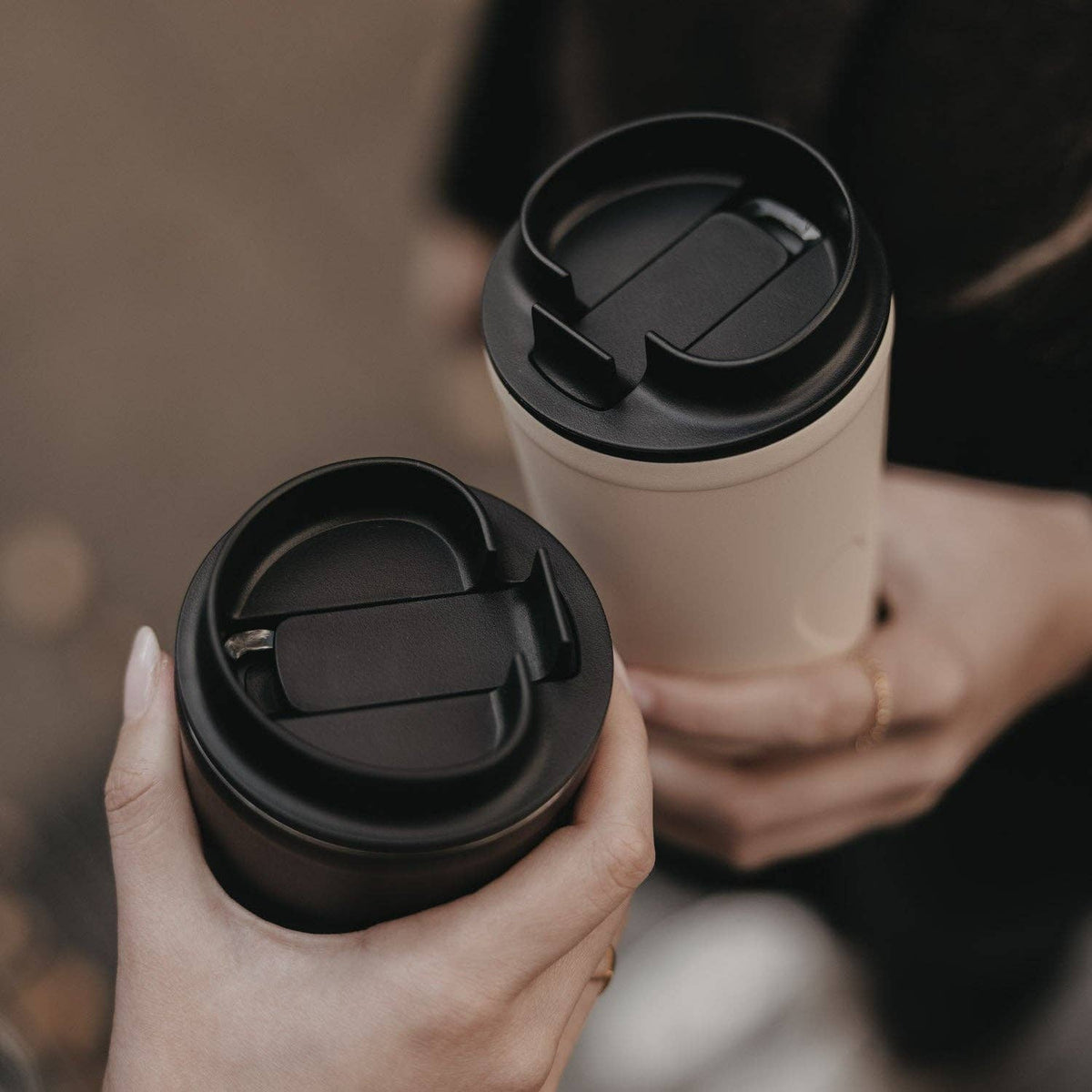 Top view of black drinking lids on cream and black travel cups held side by side.