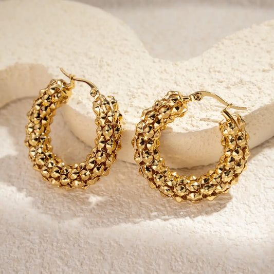 Textured gold hoop earrings with a woven design, displayed on a light decorative surface.