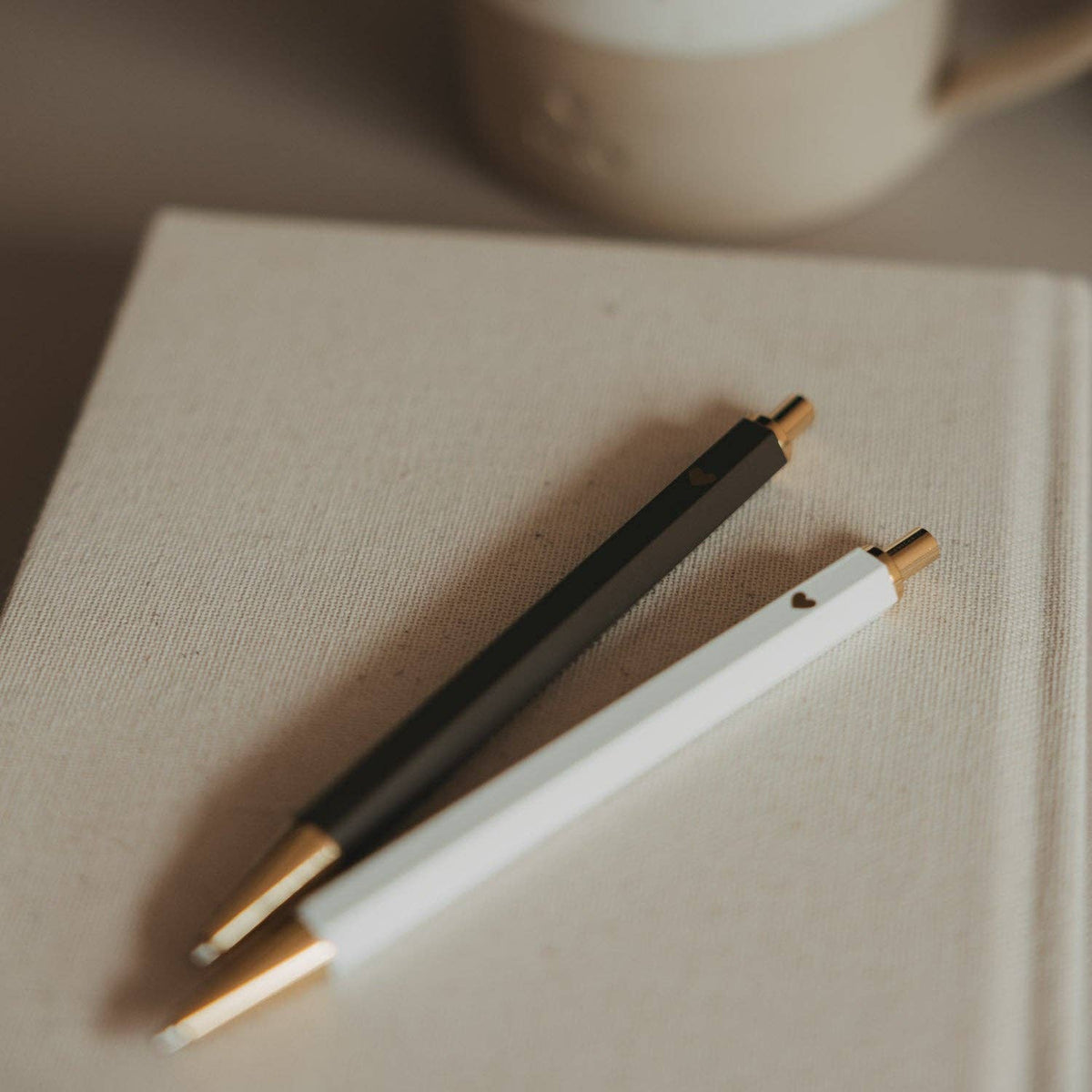 Brown and white Eulenschnitt ballpoint pens with gold-tone details resting together on a notebook.