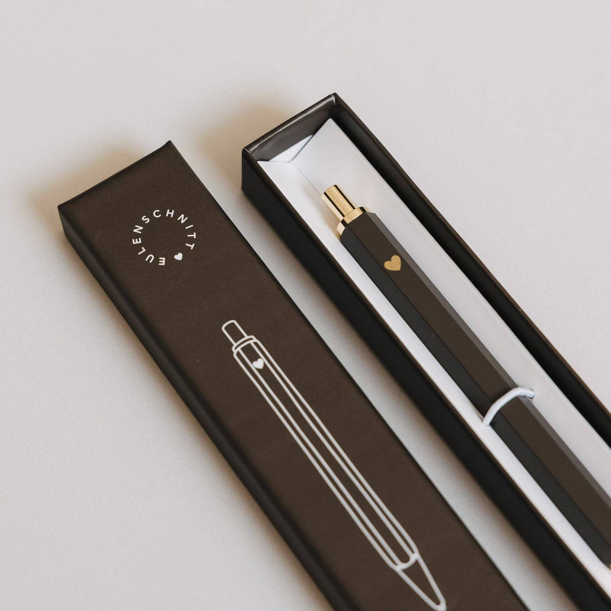 Brown Eulenschnitt ballpoint pen with a gold-coloured heart in an open presentation box beside its lid.