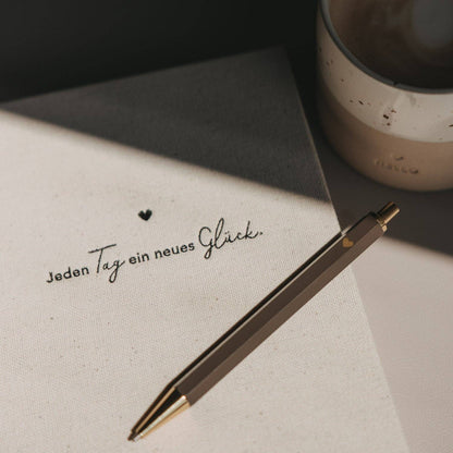 Brown Eulenschnitt ballpoint pen resting on a notebook beside a handwritten German message and a mug.