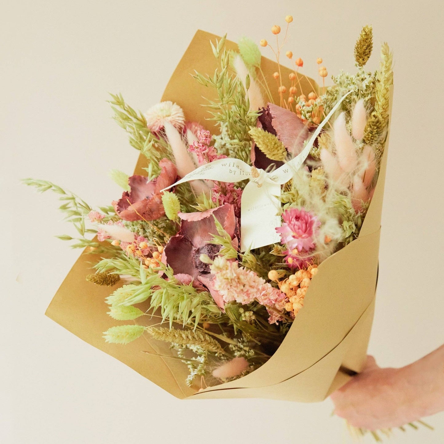 Bouquet of flowers wrapped in brown paper held by a person against a light background