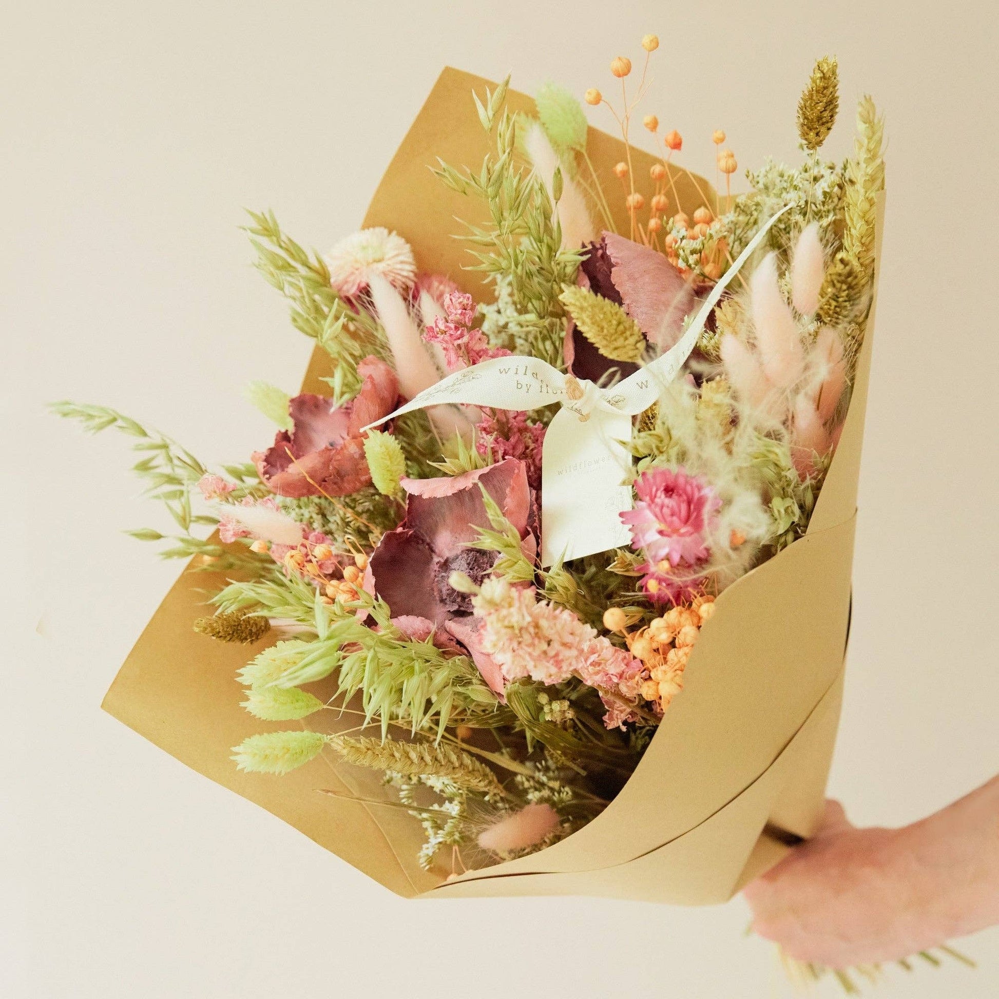Bouquet of flowers wrapped in brown paper held by a person against a light background