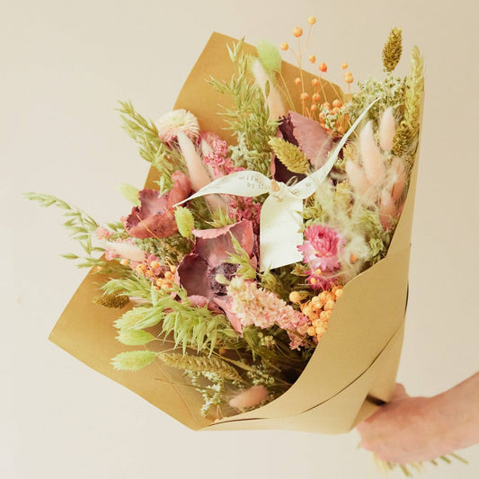 Bouquet of flowers wrapped in brown paper held by a person against a light background