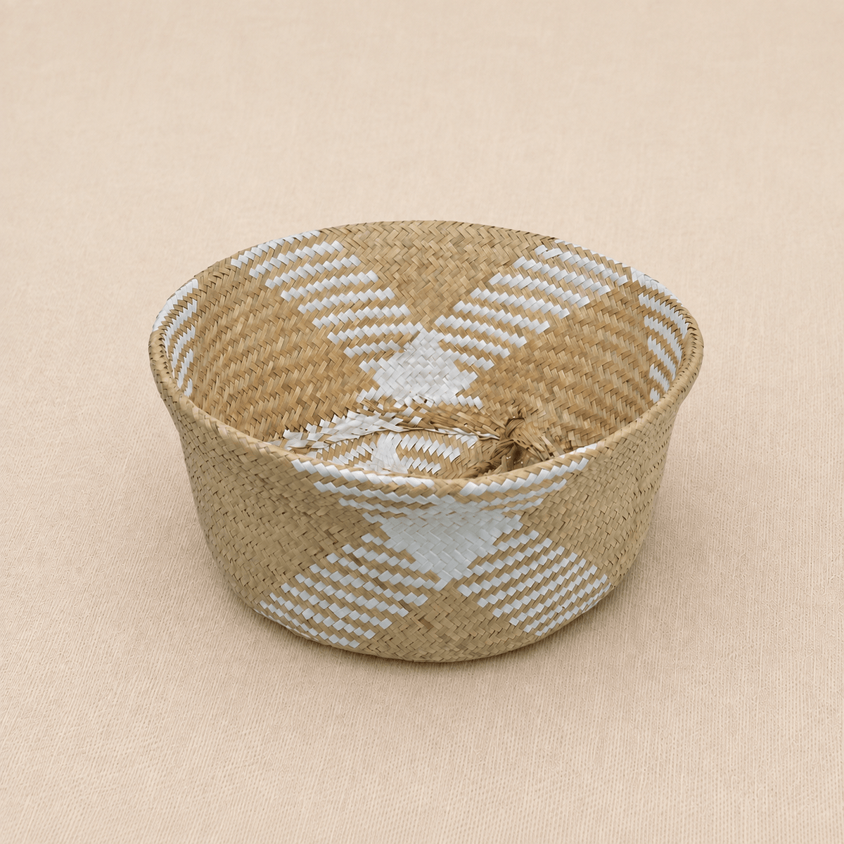 Handwoven natural seagrass baby basket with white geometric detailing on a soft