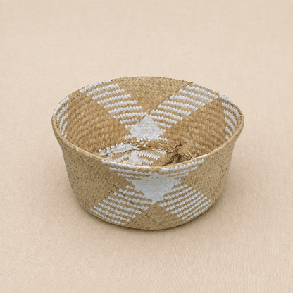 Handwoven natural seagrass baby basket with white geometric detailing on a soft
