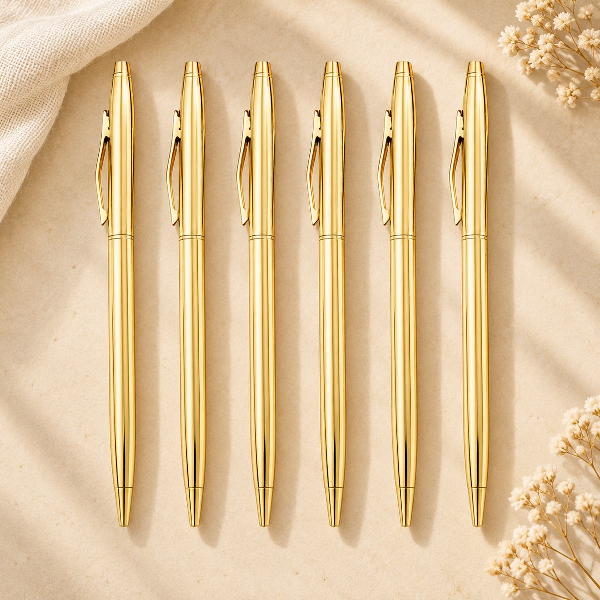 Set of six slim gold ballpoint pens with matching gold clips arranged on a warm beige background.